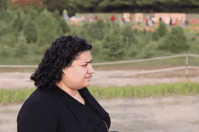 a woman in a black shirt is standing in front of a field of trees