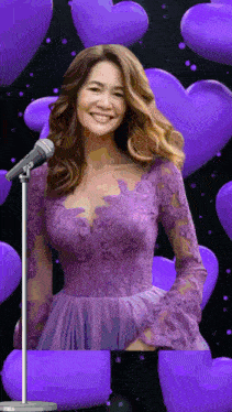 a woman in a purple dress singing into a microphone with purple hearts in the background