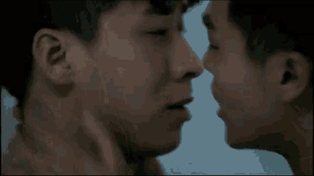 two men are kissing each other in a bathroom in a close up of their faces .