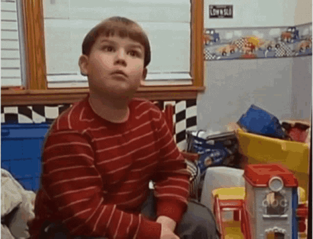 a young boy in a red striped shirt is sitting in a room filled with lots of toys
