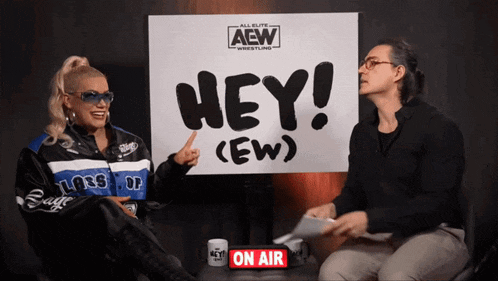 a man and a woman sit in front of a sign that says hey