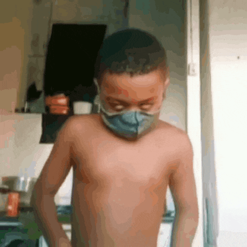 a shirtless young boy wearing a mask in a kitchen .