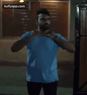 a man with a beard is wearing a blue t-shirt and adjusting his shirt .