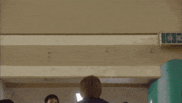 a man squatting on another man 's lap in a gym with a sign that says ' emergency exit '