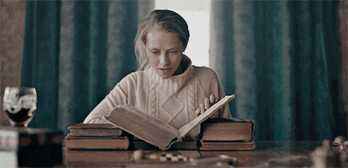 a woman in a sweater is reading a book while sitting at a table .