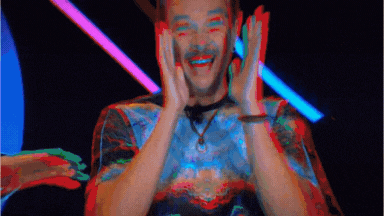 a man in a tie dye shirt is covering his face with his hands and smiling