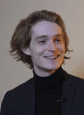 a man in a suit and turtleneck is smiling