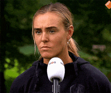 a woman stands in front of a microphone that says nos