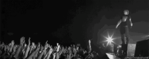 a black and white photo of a man standing on a stage in front of a crowd .