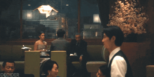 a man in a vest is talking to a woman in a diner and the words decider are on the bottom right