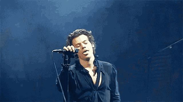 a man in a black shirt is singing into a microphone on stage .