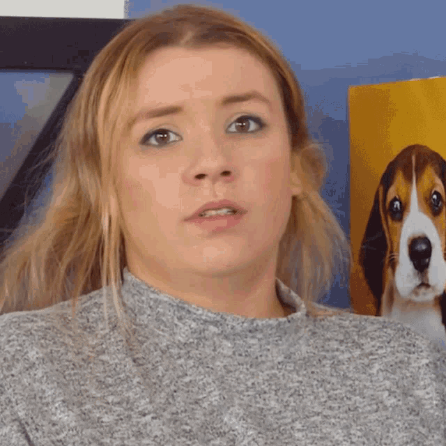 a woman in a grey sweater stands in front of a picture of a beagle