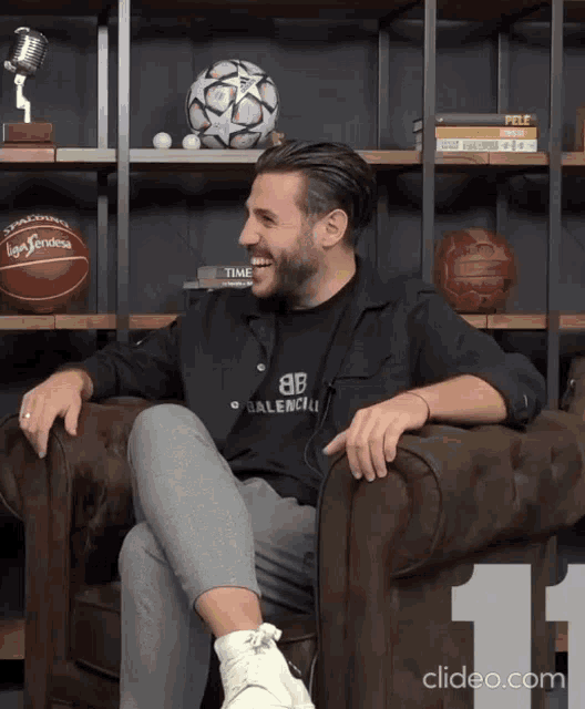 a man wearing a black balenciaga shirt sits on a couch