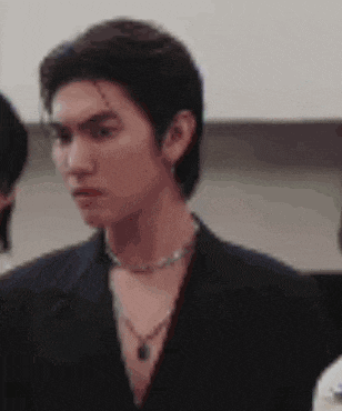 a close up of a man wearing a necklace and a black jacket .