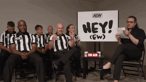 a group of aew referees are sitting in front of a sign that says hey
