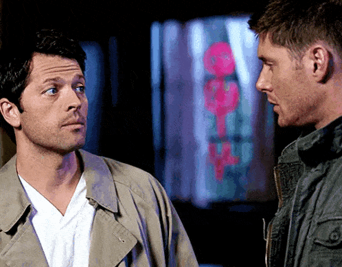 two men are standing next to each other and looking at each other with a sign in the background that says " open "