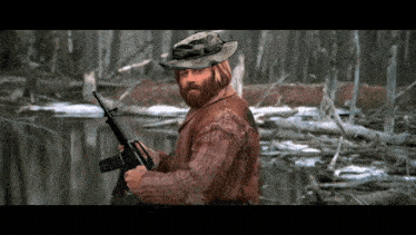 a man with a beard is holding a gun in a swamp