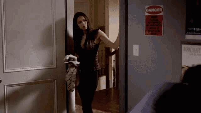 a woman is standing in front of a door with a danger sign on it .