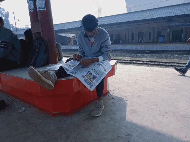a man sits on a bench reading a newspaper which says metro