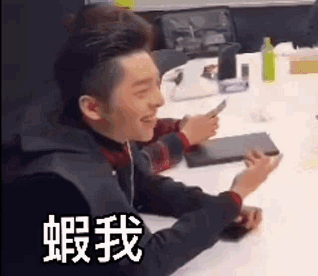 a man is sitting at a table holding a cell phone and smiling .
