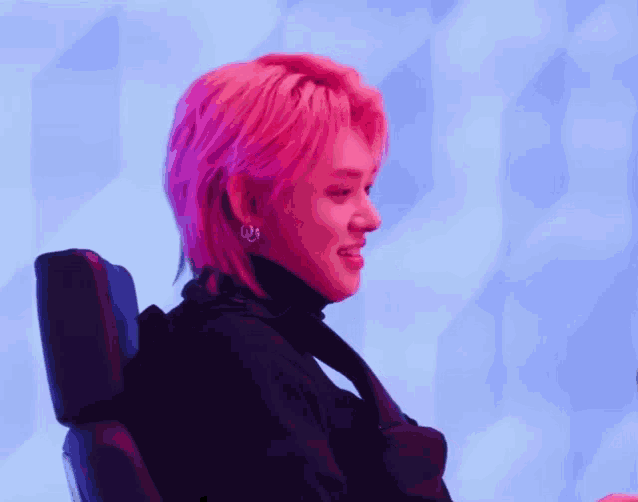 a man with pink hair is sitting in a chair and smiling