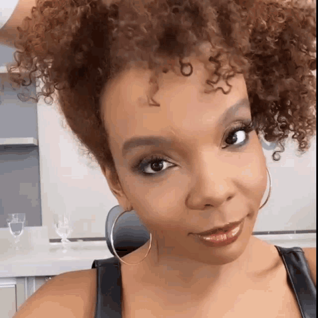 a woman with curly hair is wearing hoop earrings and a black tank top