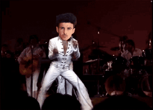 a man in a white suit is dancing on a stage in front of a band