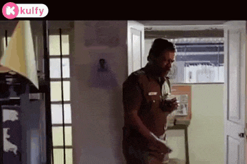 a man in a police uniform is standing in a kitchen holding a glass of water .