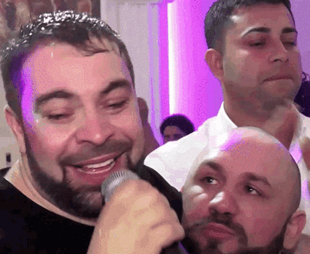 a man with a beard is singing into a microphone while two other men look on