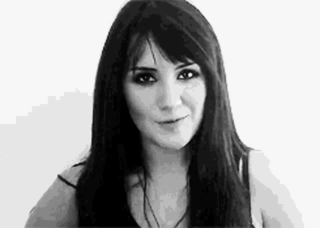 a black and white photo of a woman with long hair looking at the camera .