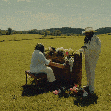 a man in a cowboy hat is standing next to a man playing a piano