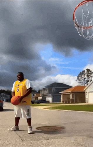 a man wearing a lakers jersey holds a basketball