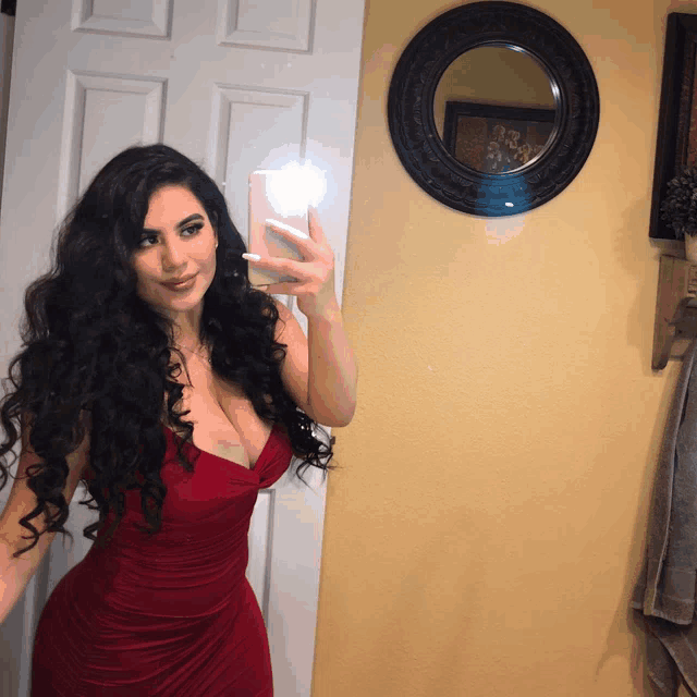 a woman in a red dress is taking a picture of herself in front of a mirror