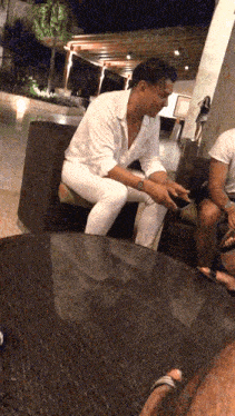 a man in a white shirt is sitting on a chair looking at his phone