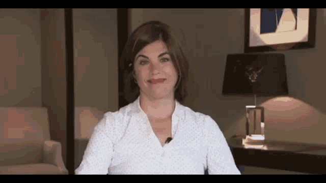 a woman in a white shirt with a microphone on her neck is smiling .
