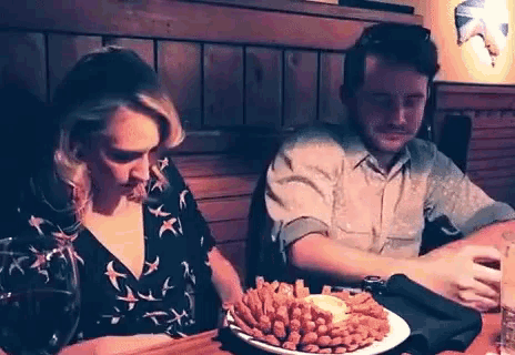 a man and a woman are sitting at a table with a plate of onion rings on it .