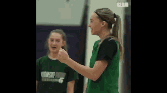 a woman in a green vest is giving a thumbs up to another woman in a green shirt .