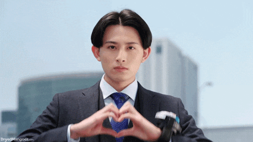 a man in a suit making a heart shape with his hands