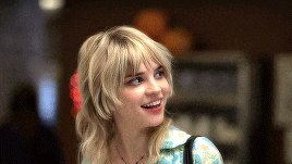 a woman with blonde hair and a flower in her hair smiles