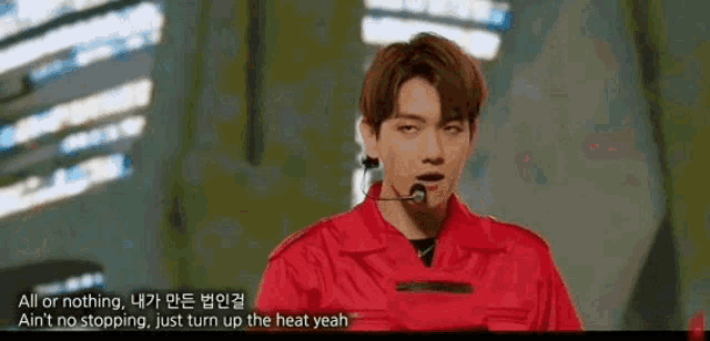 a young man in a red jacket is standing in front of a microphone on a stage .