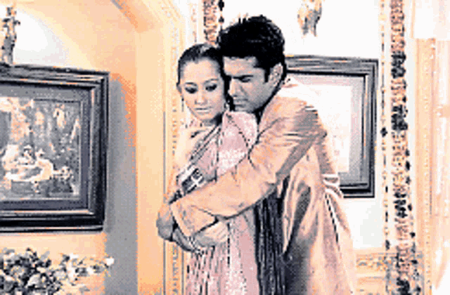 a man is hugging a woman in a room with framed pictures on the wall