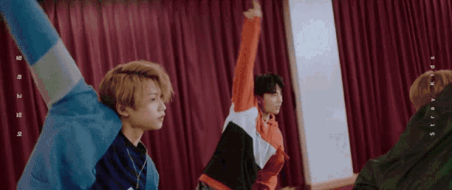 a group of young men are standing in front of a red curtain and the words stray kids are on the bottom