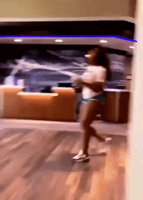 a woman in a white shirt and green shorts is walking on a wooden floor