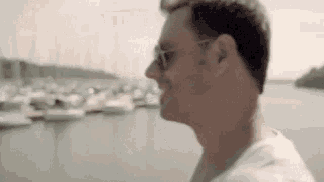 a man wearing sunglasses and a white shirt is standing in front of a body of water .