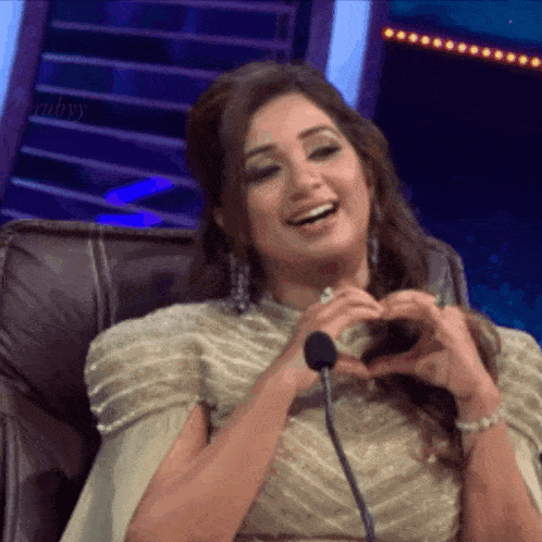 a woman is sitting in front of a microphone making a heart with her hands .