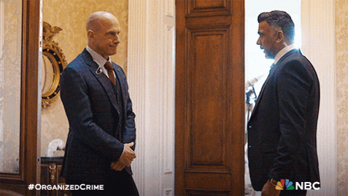 two men in suits are shaking hands in front of a door that says organized crime on the bottom