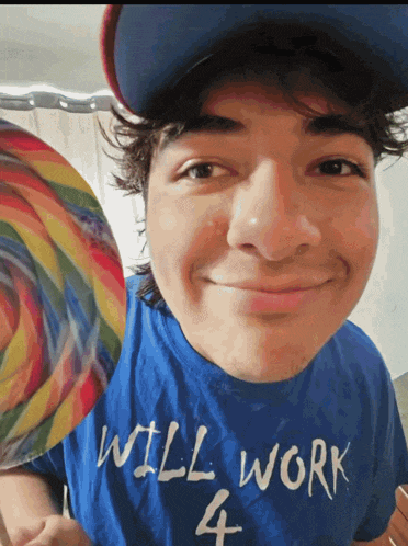 a young man wearing a blue shirt that says will work 4 holds a lollipop