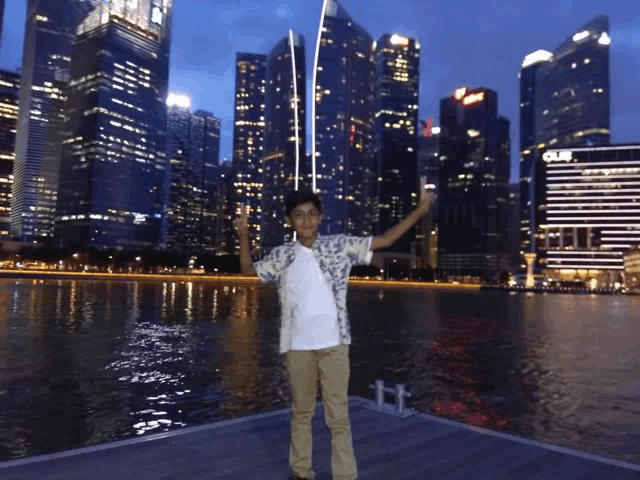 a boy stands on a dock in front of a city skyline with a building that says ' gulf ' on it