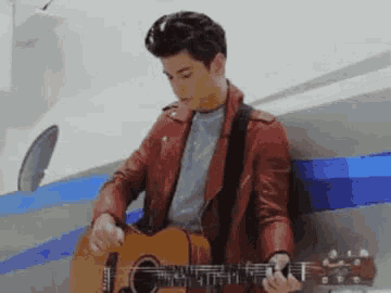 a man in a red jacket is playing an acoustic guitar .