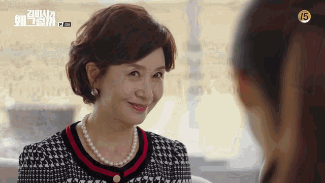 a woman wearing a pearl necklace and a plaid dress smiles